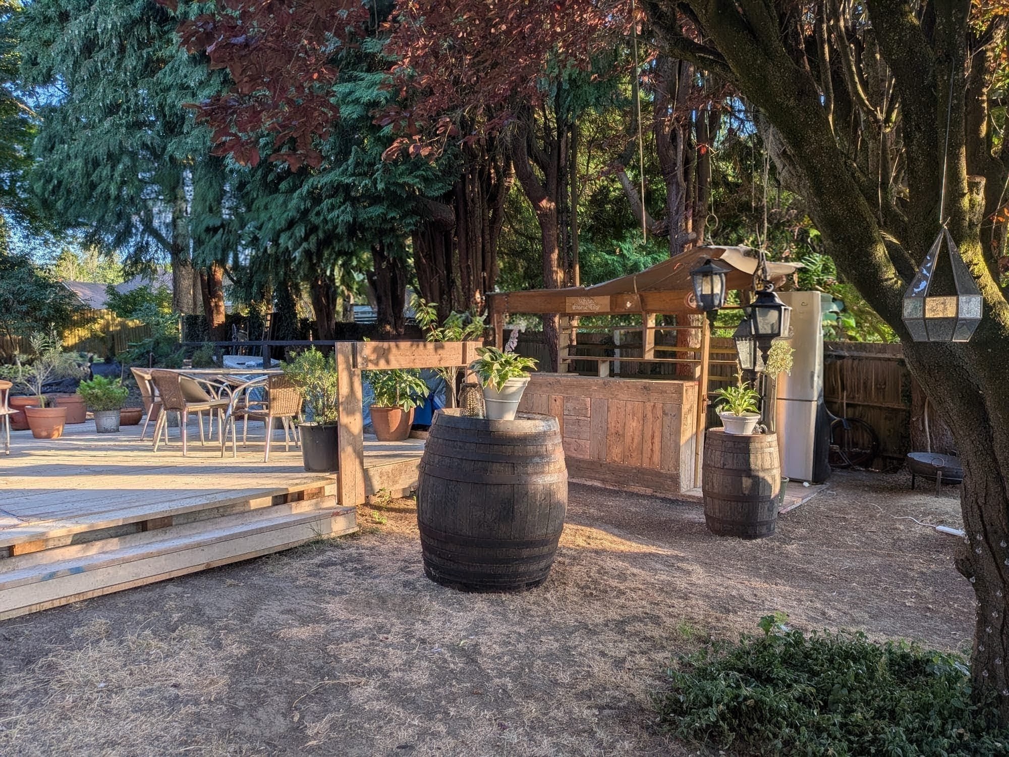 A handcrafted wooden garden bar set in a sunny garden with deck, barrels and planters
